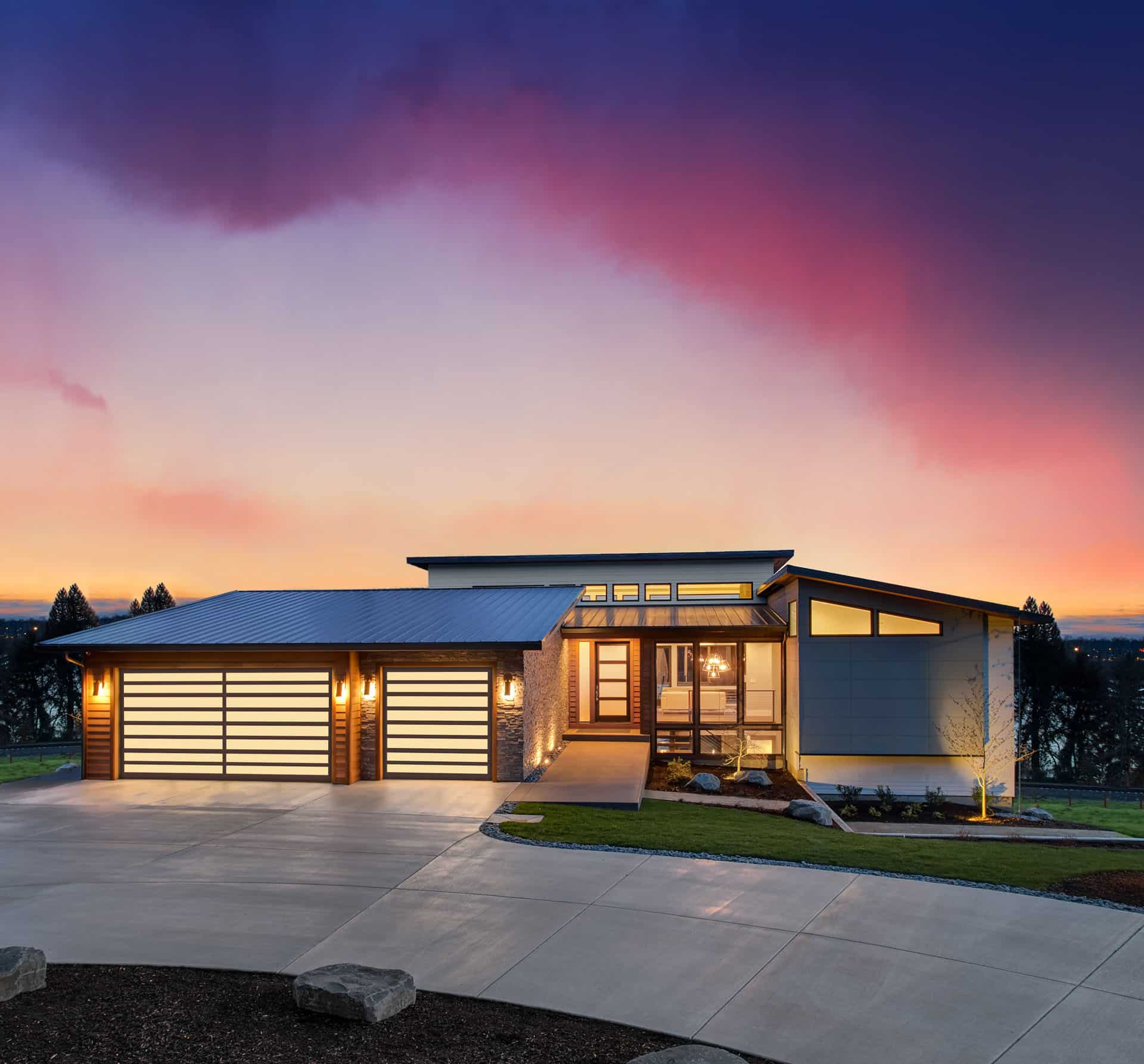 Beautiful modern luxury home exterior at sunset. Features contemporary design and three car garage