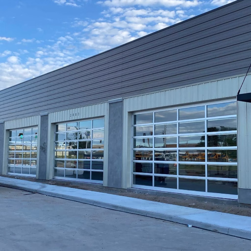 Exterior of a modern industrial building featuring full-view glass bay doors requiring Commercial Overhead Door Maintenance.