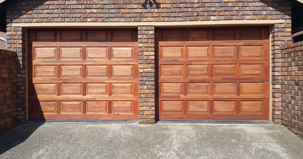 Two paneled wood garage doors with bricks.